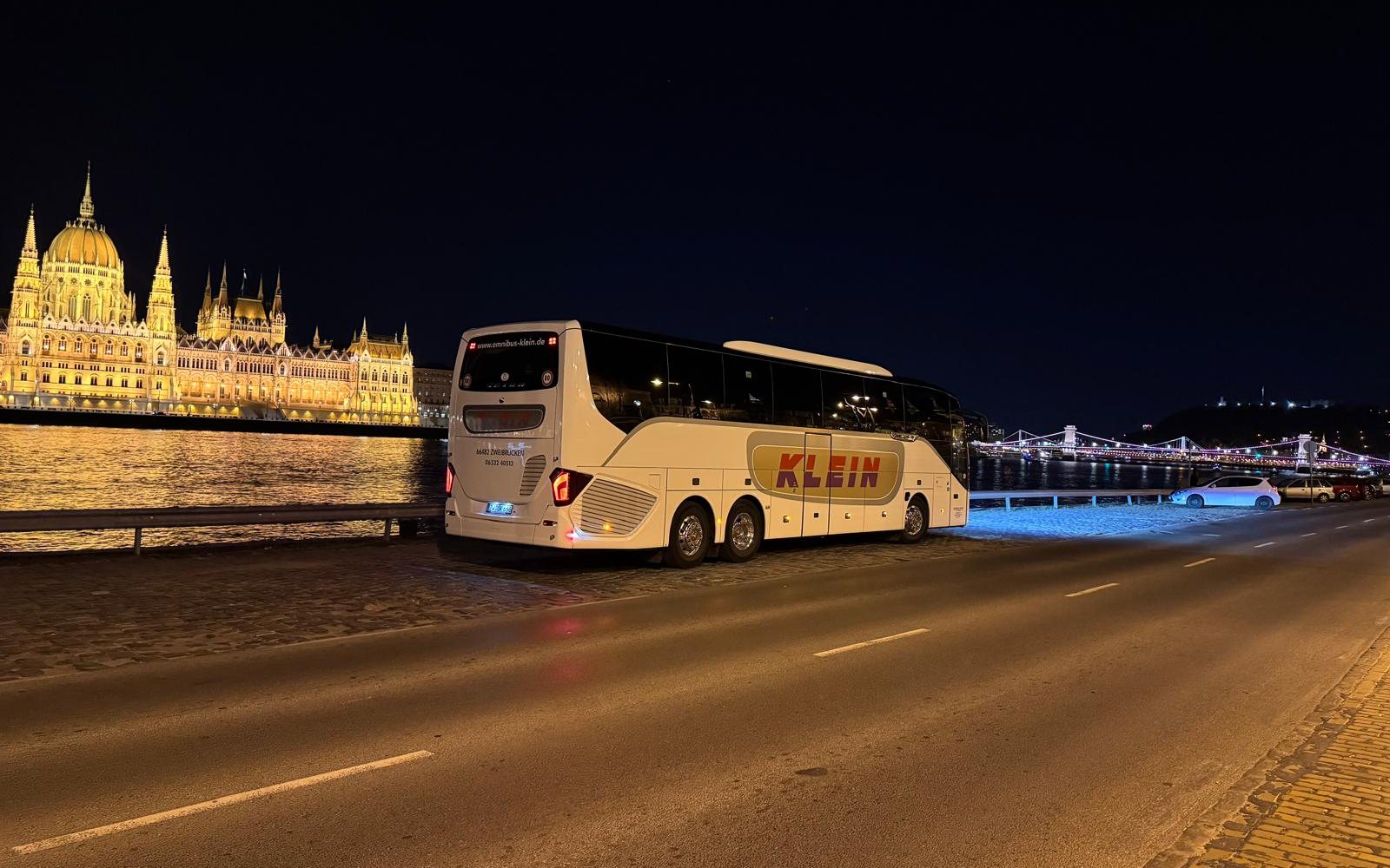 Reisebus von Omnibus Klein bei Nacht an der Donau vor dem beleuchteten Parlament in Budapest